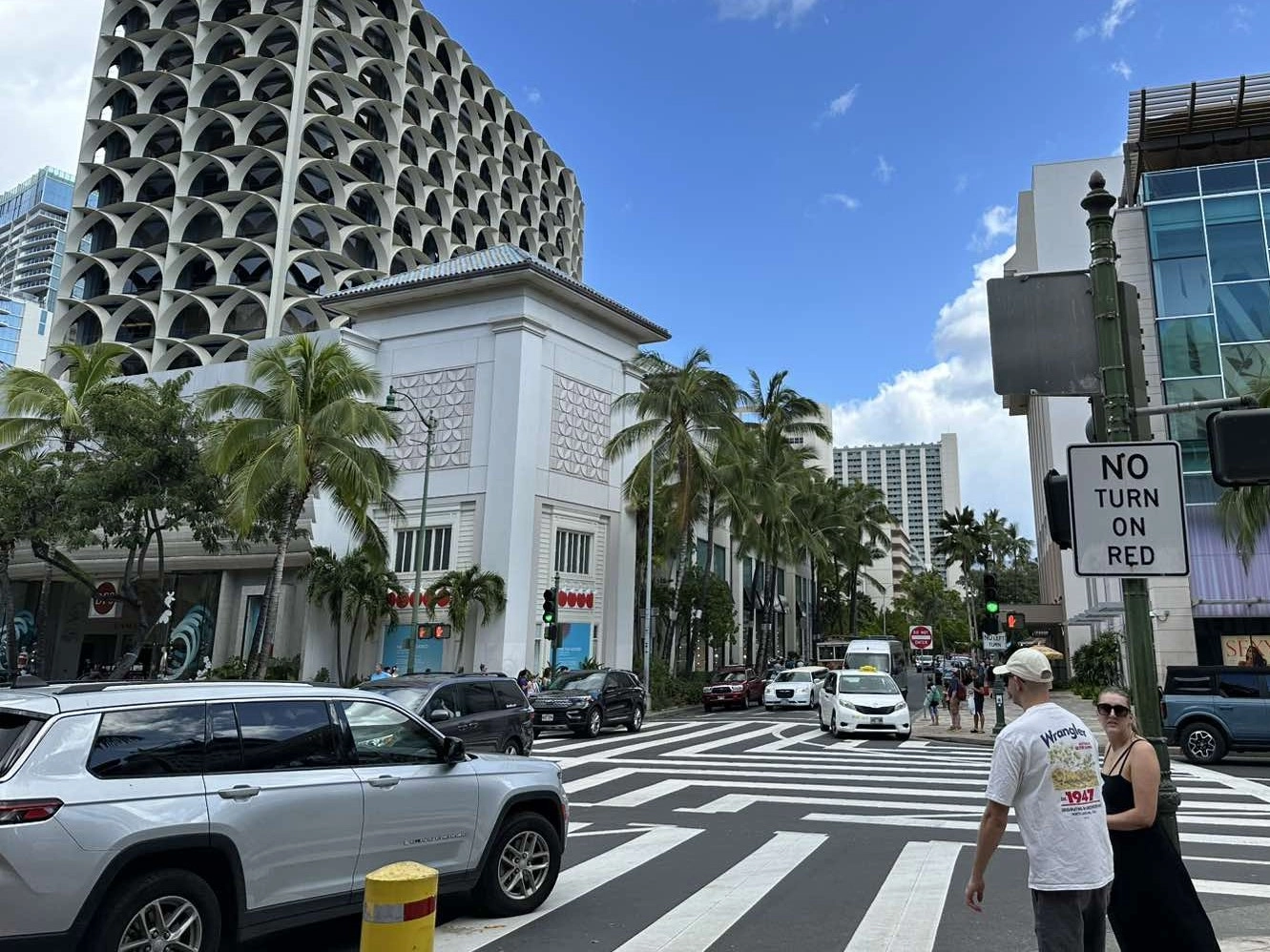 ハワイの街中の交差点風景。横断歩道や車、ヤシの木が写る、晴れた日常的なシーン。