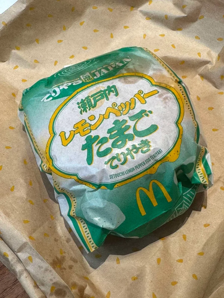 包み紙で包んだ瀬戸内レモンペッパーたまごてりやきバーガーを木製トレー上で撮影したアップ実物写真